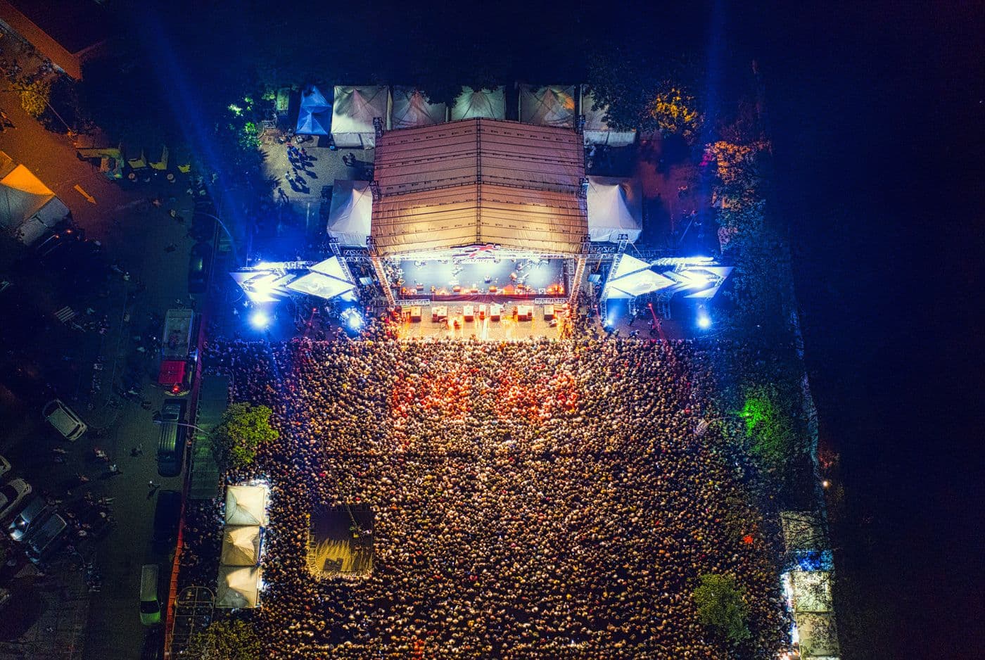 Vue aérienne d'un concert en plein air : une scène éclairée et une foule dense massée devant, de nuit